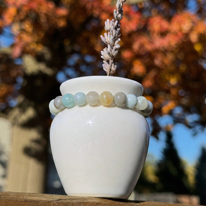 White vase with an amazonite bracelet on top against a blurred autumn tree background